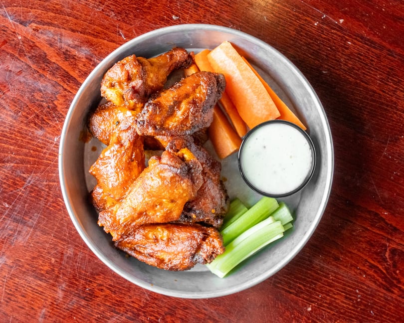 A metal tray of crispy chicken wings with carrot sticks, celery, and a side of ranch dressing.