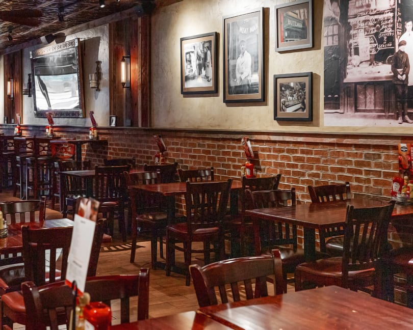 Interior of a restaurant with dark wooden tables and chairs, brick walls, and framed pictures.