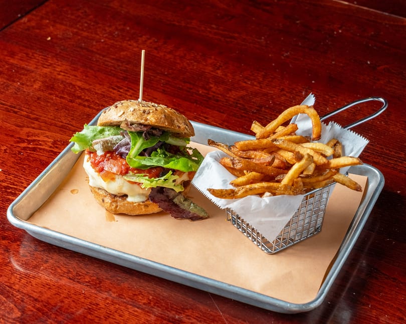 A burger with lettuce, tomato, and cheese, served with a side of fries on a metal tray.