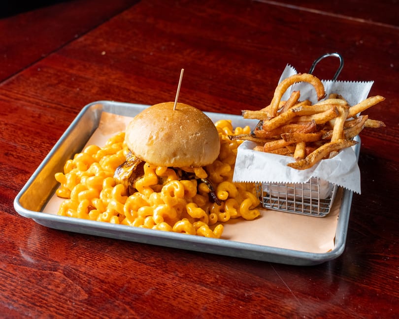 A mac and cheese burger with fries in a metal basket, served on a tray.
