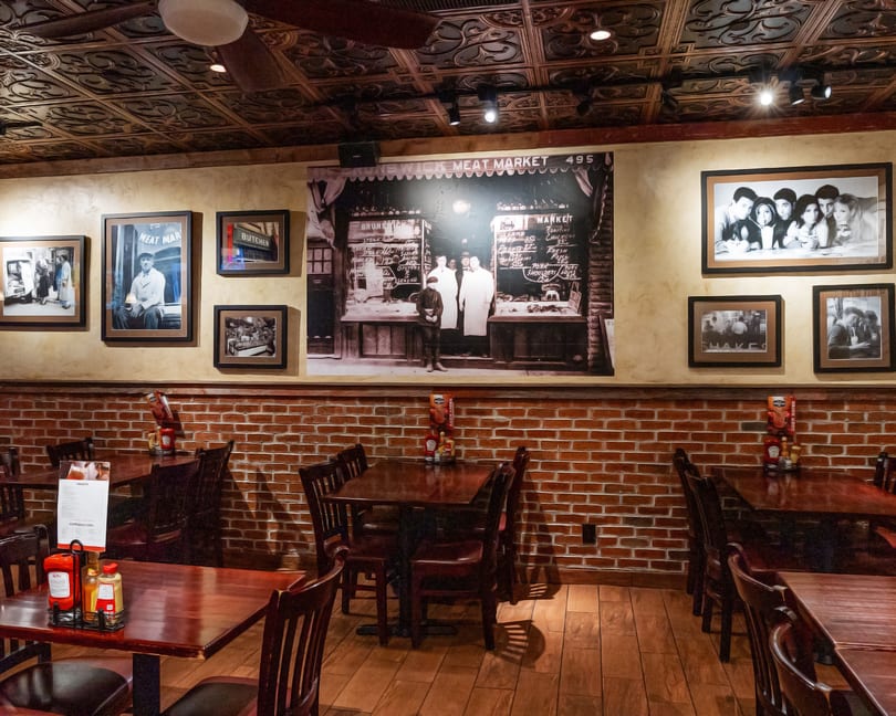 Restaurant interior with dark wooden tables and chairs, brick walls, and vintage framed photos.