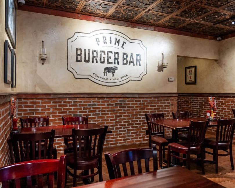 Interior of Prime Burger Bar with a large logo, brick walls, dark wooden tables, and chairs.